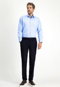 Lichtblauwe overhemd met lange mouwen, marineblauwe broek en donkere instapschoenen. Gladde texturen en een getailleerde pasvorm zijn duidelijk zichtbaar.