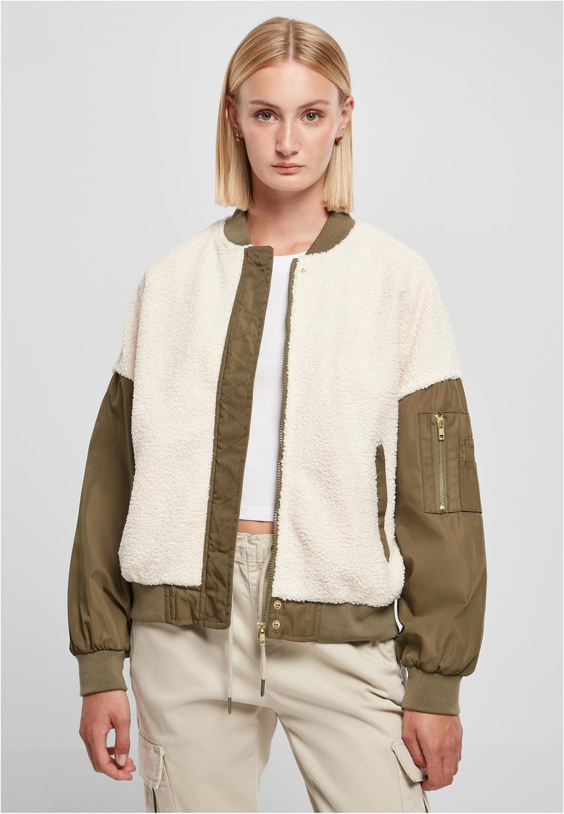 Veste bombardier avec un devant en polaire crème et moelleux, et des manches matelassées vert olive. Elle dispose de poignets côtelés et d'une poche zippée sur le bras.