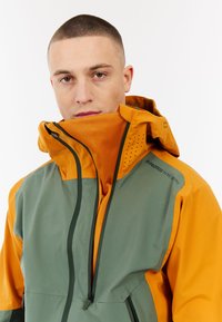 Waterdichte jas in groen en oranje, met een ritsluiting, capuchon en meshpanelen voor ventilatie. Duurzame stof met textuuraccenten.