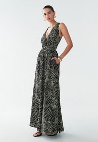 Mono negro con escote en V profundo, lazo ajustable en la cintura y diseño de ondas amarillas. Piernas acampanadas y bolsillos incluidos.