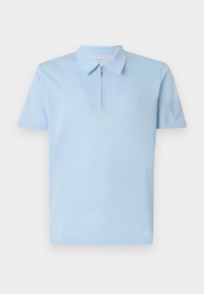 Polo azul claro feito de tecido suave, com meia abertura e colarinho estruturado. Mangas curtas com um acabamento limpo na bainha.