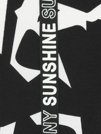 Schwarz-weiß gemusterter Stoff mit auffälligen Formen. Ein vertikales Band mit dem Text "NY SUNSHINE" ist auffällig in Weiß dargestellt.