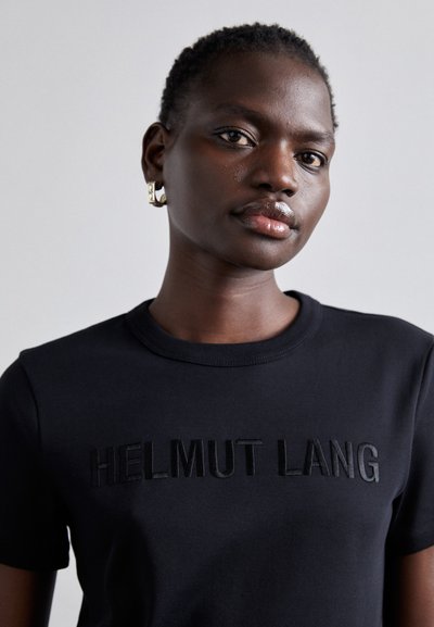 Camiseta preta de algodão com gola redonda e um logótipo bordado "HELMUT LANG" em acabamento mate tonal. Textura lisa, mangas curtas.