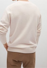 Jasnoróżowy sweter wykonany z miękkiego materiału, z prążkowanym ściągaczem u dołu i na mankietach, z klasycznym okrągłym dekoltem i luźnym krojem, zestawiony z beżowymi spodniami.