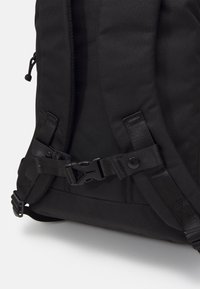 Mustasta kankaasta valmistettu reppu, jossa säädettävät hihnat, solkikiinnitys ja vahvistettu ompelu. Päällä sileä pinta ja minimalistinen muotoilu.