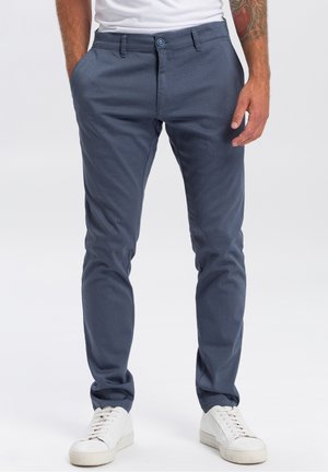 Marineblauwe getextureerde broek met een slim fit, voorzien van zijzakken en een knoopsluiting, gecombineerd met witte sneakers.