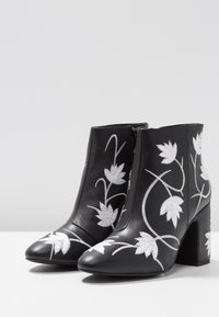 Botas de tobillo de cuero negro con bordado de hojas plateadas, punta afilada y tacón cuadrado. Cierre con cremallera lateral para facilitar su uso.