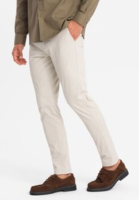 Pantalones de algodón beige con corte ajustado, que cuentan con bolsillos laterales y una textura suave, combinados con zapatos de ante marrones y una camisa de botones.