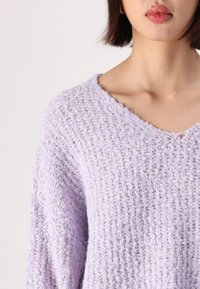 Sweater lilás de malha com um corte solto, design em V, padrão texturizado e material suave e fofinho. Proporciona um aspeto relaxado e confortável.