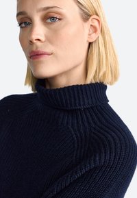 Jersey de cuello alto de punto acanalado azul marino con un acabado texturizado, que presenta un cuello alto y un corte ajustado.