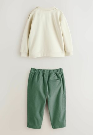 Sweatshirt color crema chiaro con polsini e scollo a costine, abbinato a pantaloni jogger in cotone verde con vita elasticizzata e tasca laterale.