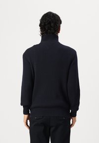 Marineblauer gerippter Rollkragenpullover mit langen Ärmeln, lockerer Passform und strukturiertem Muster. Hergestellt aus Strickstoff und mit hohem Kragen.