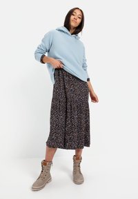 Helles blauer Hoodie mit Kapuze, über einem dunklen, floral bedruckten Kleid geschichtet. Beigefarbene Schnürstiefel. Strukturiert, lässige Passform und gestuften Rockdesign.