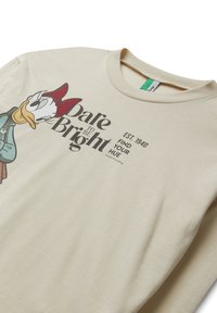 Sudadera beige con cuello redondo, que presenta un gráfico de un personaje de dibujos animados en la parte delantera y el texto: "Atrévete a ser Brillante. EST 1940, ENCUENTRA TU TONO."