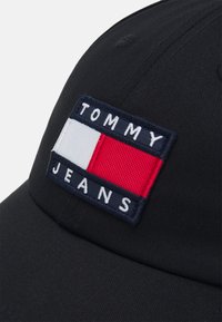 Cappellino da baseball nero con un'etichetta ricamata rettangolare con le parole "TOMMY" e "JEANS", insieme a un design rosso e bianco.