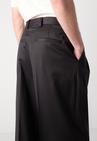 Schwarze maßgeschneiderte Hosen mit einer glatten Textur, flachen Taschen und einem geraden Schnitt. Der Bund hat Gürtelschlaufen zur Anpassung.