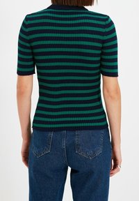 Haut à manches courtes côtelé avec des rayures horizontales vert foncé et bleu marine. Associé à un jean denim bleu à coupe décontractée, vue de dos et détails visibles.