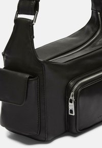 Sac en cuir noir avec une texture lisse, comportant un compartiment principal zippé, une poche avant et une bandoulière réglable avec quincaillerie en métal.
