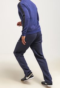 Felpa blu navy con pannelli laterali neri e pantaloni coordinati. Presenta un tessuto texturizzato e polsini a coste. Indossata con scarpe da ginnastica nere.