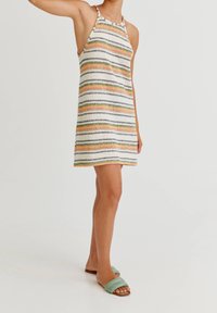 Robe sans bretelles avec des rayures multicolores en orange, vert et noir sur fond blanc. Fabriquée en tissu l éger, de longueur au-dessus du genou.