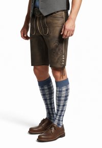 Pantaloni corti in pelle marrone con ricami decorativi, abbinati a calze al ginocchio a scacchi blu e bianche e scarpe marroni. Presenta tasche laterali e bottoni.