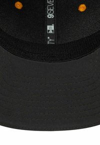 Czarny kapelusz z płaskim wizjerem, ozdobiony żółtymi przeszyciami i teksturowanym wnętrzem. Etykiety zawierają rozmiar oraz instrukcje dotyczące pielęgnacji.