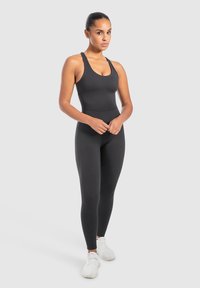Zwarte sportieve bodysuit met een gladde, rekbare textuur, voorzien van brede bandjes en een nauwsluitende snit, gecombineerd met witte sneakers.