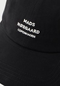 Black cotton baseball cap featuring embroidered text "MADS NØRGAARD COPENHAGEN." Smooth texture with curved brim and stitched detailing.