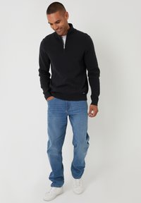 Czarna rozpinana bluza z dzianiny, połączona z jasnoniebieskimi dżinsami. Modelka stoi w luźnej pozach, nosząc białe sneakersy.
