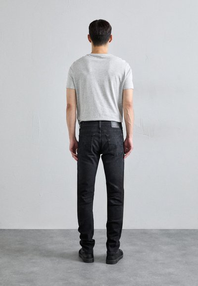 Grå t-shirt för män, svarta jeans och svarta sneakers sedd bakifrån, med en enkel, avslappnad passform och rak ben-design.