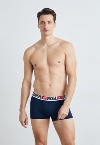 Sous-vêtements bleu marine avec une ceinture logo blanche et rouge contrastante. La coupe est ajustée avec une texture douce et lisse, conçue pour le confort.