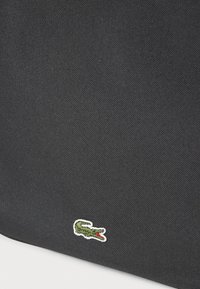 Black textured fabric bag featuring a green and white crocodile logo embroidered on the lower corner. Compact rectangular shape.