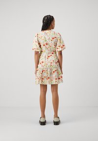 Rochie cu imprimeu floral, cu mâneci bufante, talie strânsă și tiv în straturi. Prezintă flori colorate pe un fundal deschis. Este purtată cu pantofi gri.
