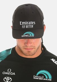 Cappello nero con la scritta "Emirates FLY BETTER" in bianco, logo ricamato in turchese. Visiera corta, materiale leggero, progettato per l'abbigliamento sportivo.