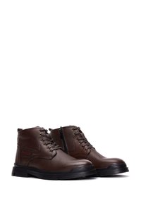 Botas de cuero marrón hasta el tobillo con un acabado texturizado, punteras redondas, ojales de metal y una cremallera lateral para facilitar su uso. Suelas de goma para mayor tracción.