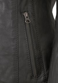 Schwarze Lederjacke mit einem silbernen YKK-Reißverschluss, sichtbaren Nähten und einer glatten Textur in körperbetontem Design.