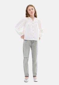Vit långärmad blus med knäppning fram och volang i halsen, kombinerad med ljusgrå ripped jeans och silverfärgade ballerinan.