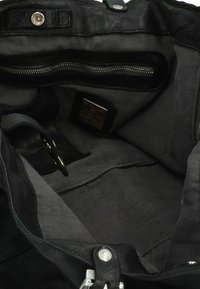 Interno di una borsa a mano in pelle nera con una fodera in tessuto grigio, una tasca con zip, accessori metallici e doppi ganci.