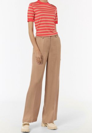 Kvinde iført koral- og lyserøget striped kortærmet skjorte, beige vidbenede bukser og creme chunky loafers med guldkæde detalje.