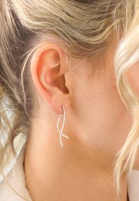 Silberfarbene Ohrringe mit einem gedrehten Design, die kleine, klare Strasssteine entlang der Kurven aufweisen und nahe am Ohrläppchen hängen.