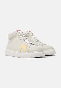 High-top sneakers in light beige suede with a yellow leather accent, white rubber sole, and white laces. Red branded logo on the tongue.