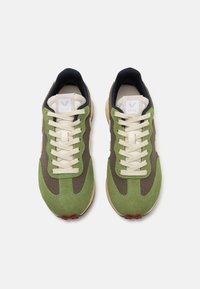 Grønne og brune sneakers med en kombinasjon av semsket skinn og mesh, rund tå, snøring og en hvit logo-patch på tungen. Gummisåle med teksturerte detaljer.