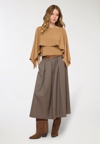 Maglione beige a strati con maniche larghe, abbinato a gonna plissettata con motivo pied de poule. Cintura marrone con fibbia rotonda e stivali marroni al ginocchio.