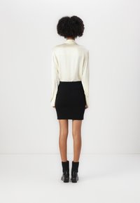 Bluză de mătase, crem, cu mâneci lungi, asortată cu o fustă din tricot neagră, ajustată. Întreaga ținută include ghete negre până la gleznă, cu detalii crețate.
