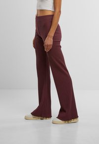 Pantalons évasés côtelés bordeaux avec une taille élastique, texture douce et silhouette ajustée, associés à des baskets blanches.