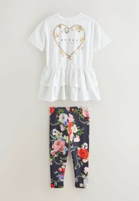 Biely viacvrstvový peplum top s dizajnom srdca a zlatými akcentmi, v kombinácii s čiernymi legínami s kvetinovým vzorom a živými viacfarebnými motívmi.