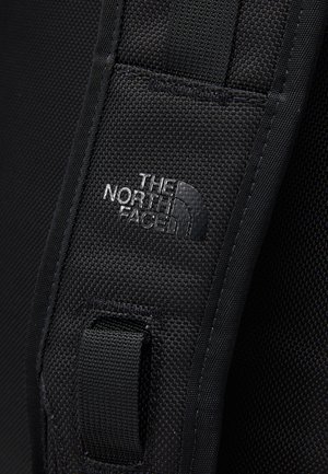 Sort rektangulær North Face rygsæk med lodret logo, dobbeltrumslukning på toppen og sidelommer med kompressionsstropper på en ensfarvet baggrund.
