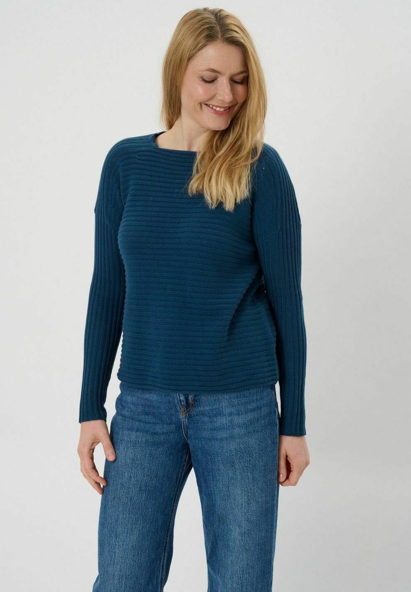 Teal geribbelde trui met lange mouwen, ronde halslijn en een ontspannen pasvorm, gecombineerd met lichtblauwe straight-leg jeans.