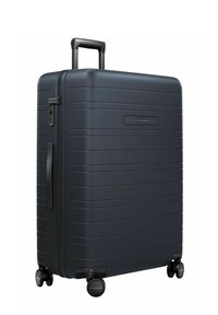 Valise rigide de couleur bleu marine foncé, arborant un design épuré avec des rainures horizontales, une poignée rétractable et quatre roues à roulement fluide.