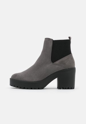 Bottine en daim gris avec panneau latéral élastique noir, talon haut et épais, semelle noire texturée sur fond blanc.